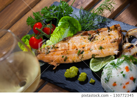 Tasty trout fillet with rice, tomatoes and greens served on black plate 130772345