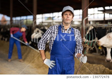 Farmer man stands with rake at cow farm Farmer man stands with rake at cow farm 130772478