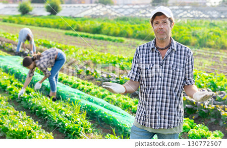 Positive man owner of plantation garden is resting standing after work and tasks. Positive man owner of plantation garden is resting standing after work and tasks. 130772507