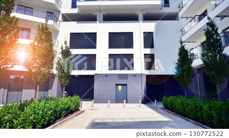 Modern apartment building with balconies and greenery. Beautiful view of real estate buildings in summer. Walking area with trees and grass. Modern residential buildings in the public green area.  130772522