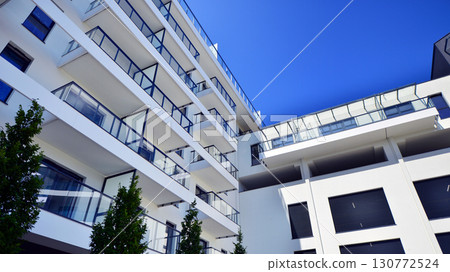 Modern apartment building with balconies and greenery. Beautiful view of real estate buildings in summer. Walking area with trees and grass. Modern residential buildings in the public green area. Modern apartment building with balconies and greenery. Beautiful view of real estate buildings in summer. Walking area with trees and grass. Modern residential buildings in the public green area. 130772524