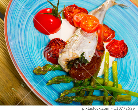 Baked fish poutassou with dried tomatoes, asparagus and creamy-garlic sauce 130772559