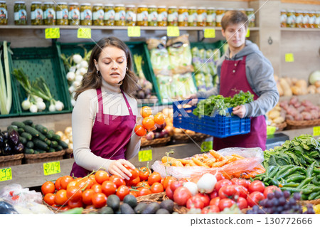 Saleswoman in an apron puts ripe tomatoes on supermarket window 130772666