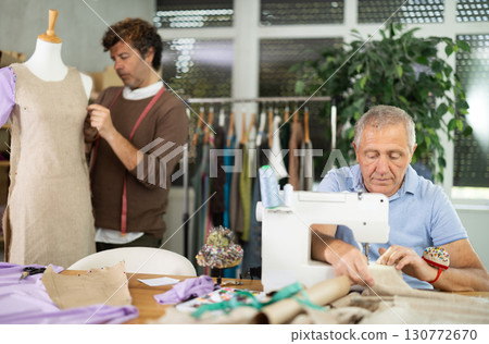 mature woman sews against the background of a tailor and a mannequin mature woman sews against the background of a tailor and a mannequin 130772670