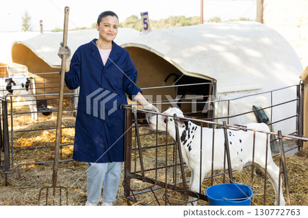 Middle-aged female farmer standing next to fencing with calf 130772763