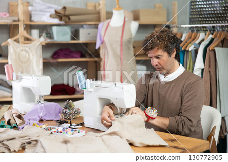 Man tailor sews on sewing machine in workshop Man tailor sews on sewing machine in workshop 130772905