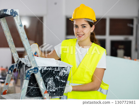 Portrait of woman painter in a protective helmet and vest with paint roller Portrait of woman painter in a protective helmet and vest with paint roller 130772981