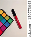 Makeup flat lay with bright eyeshadow palette and red lip gloss on white background 130773043