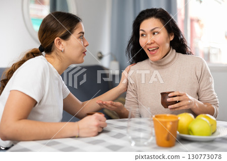 Smiling woman with cup of tea talking with girlfriend at home 130773078