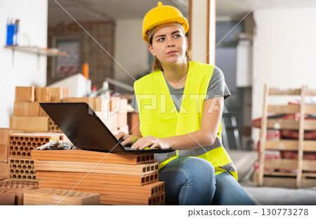 Female contractor using laptop to check plan of building under construction 130773278