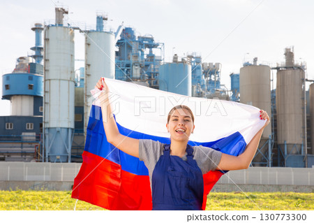 near factory in outback,jubilant female employee in overalls stands with flag of Russia near factory in outback,jubilant female employee in overalls stands with flag of Russia 130773300