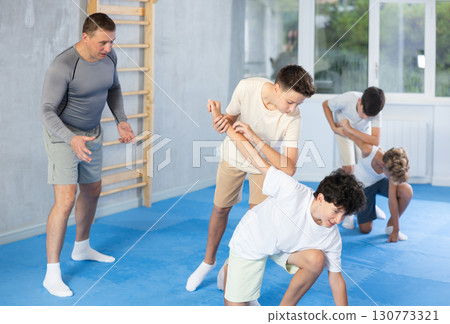 Diligent preteen student twisting his opponent's arm in sports hall Diligent preteen student twisting his opponent's arm in sports hall 130773321