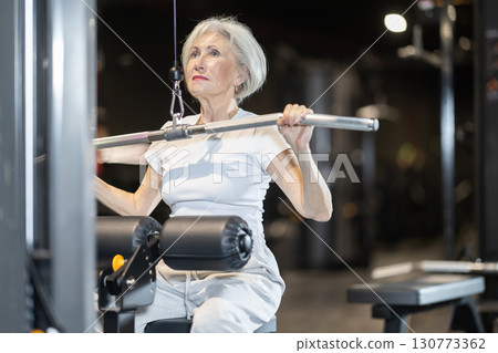 Senior woman doing wide grip lat pulldown on cable machine at gym 130773362