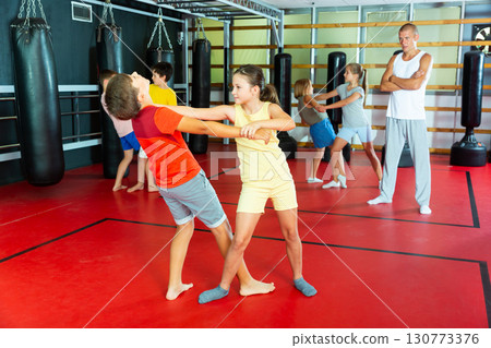 Preteen children practicing in pair self-defence movements with male trainer 130773376