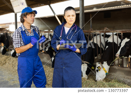 Man and Asian woman farmer with tablet talking at cowshed Man and Asian woman farmer with tablet talking at cowshed 130773397