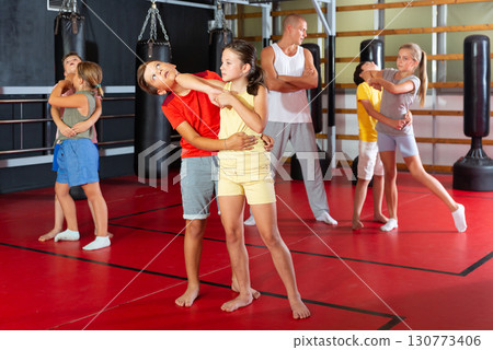Sporty girls and boys are practices self-defence moves in pairs in gym. Sporty girls and boys are practices self-defence moves in pairs in gym. 130773406