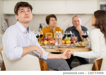 Dissatisfied guy turned away from the festive table, where his family and friends were having conversation. Quarrel during home dinner Dissatisfied guy turned away from the festive table, where his family and friends were having conversation. Quarrel during home dinner 130773409