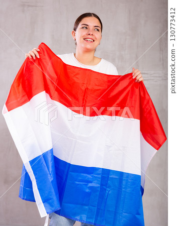 Joyful smiling young woman waving state flag of Netherlands against gray wall background Joyful smiling young woman waving state flag of Netherlands against gray wall background 130773412