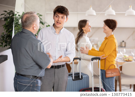 Young guy with suitcase coming back home, father welcoming son at door. Parents happy to see home, welcoming children 130773415