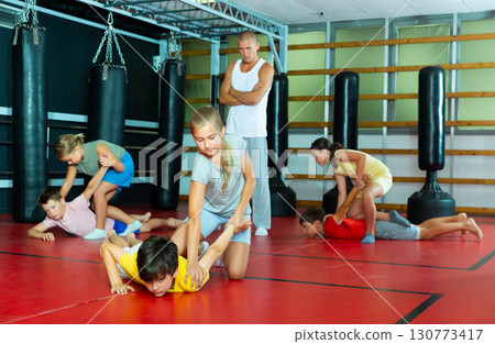 Sporty girls and boys are practices self-defence moves in pairs in gym. Sporty girls and boys are practices self-defence moves in pairs in gym. 130773417