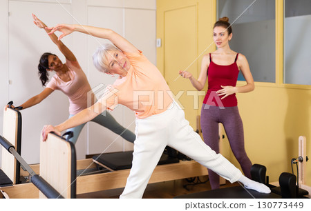 Elderly woman performing pilates exercises on reformer during group workout 130773449