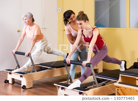 Two active women perform an exercise using a reformer bed Two active women perform an exercise using a reformer bed 130773465