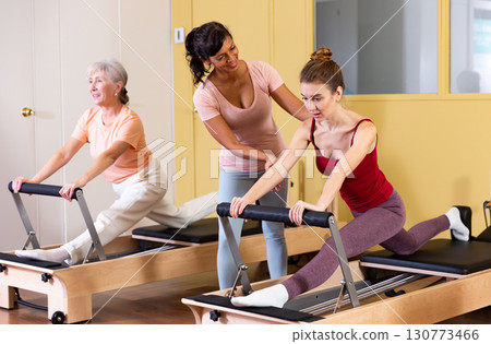 Two active women perform an exercise using a reformer bed 130773466