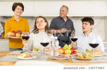 Father and mother together with adult children talking at dinner table at home 130773467