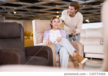 Happy couple trying out armchairs in furniture showroom 130773468