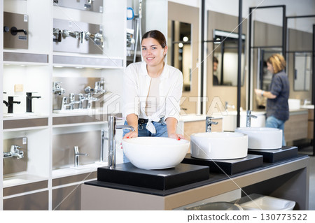 Smiling woman inspects and chooses new kitchen or bath tap faucet at hardware store Smiling woman inspects and chooses new kitchen or bath tap faucet at hardware store 130773522