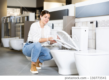 in plumbing department, female buyer checks for defects of toilet before purchasing toilet pan in plumbing department, female buyer checks for defects of toilet before purchasing toilet pan 130773541