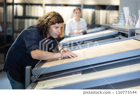 in hardware store,male buyer carefully examines laminate sample. Man chooses flooring material 130773544