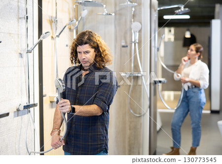 in plumbing department,man examines shower head and quality of metal coating. in plumbing department,man examines shower head and quality of metal coating. 130773545
