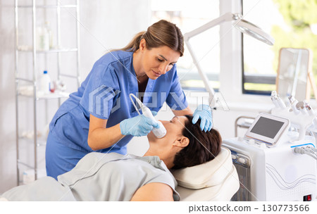 Female aesthetician administering hardware facial procedure using ice hammer on woman 130773566