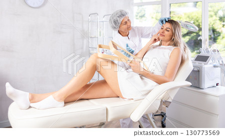 Elderly female aesthetician consulting young woman before facial treatments 130773569