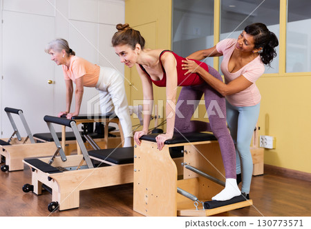 Female instructor helps women perform an exercise on a combined chair 130773571