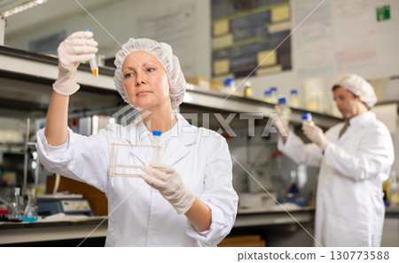 Female scientist researcher holding tripod and looking at reaction in test tube while performing biochemical tests in lab 130773588