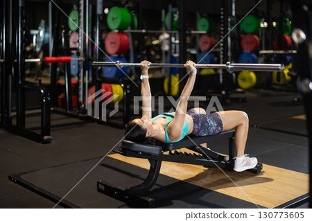 Woman performing bench chest press with barbell in gym 130773605