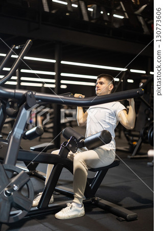 Young man training on plate-loaded lat pulldown machine at gym Young man training on plate-loaded lat pulldown machine at gym 130773606