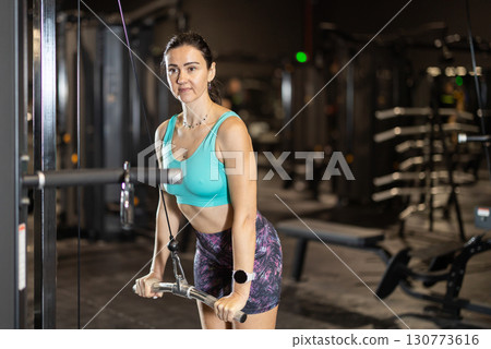 In gym, woman uses cable row machine to strengthen muscles. In gym, woman uses cable row machine to strengthen muscles. 130773616