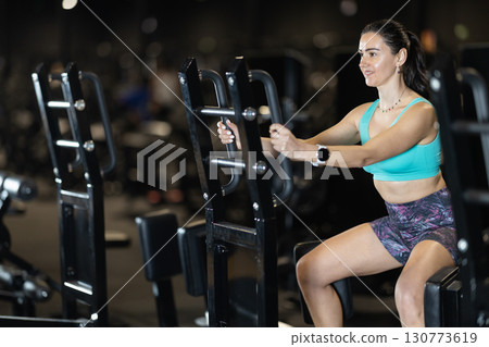 Woman training hips on standing abductor machine at gym 130773619