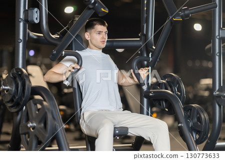 Young man exercising on chest press machine in gym Young man exercising on chest press machine in gym 130773633