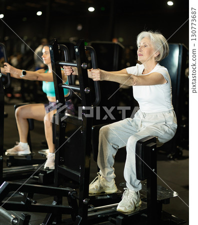 Senior woman uses leg abduction machine to strengthen muscles Senior woman uses leg abduction machine to strengthen muscles 130773687