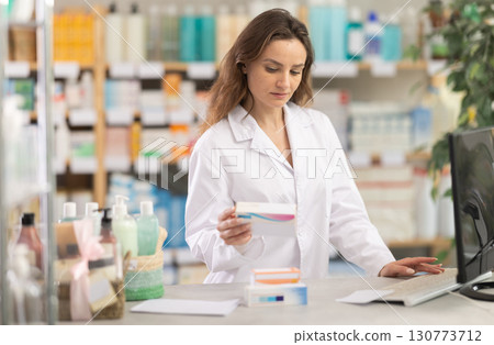 Female pharmacist standing at drugstore with medical product in hands 130773712