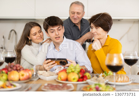 Happy parents and their children look at and discuss photos of them together on smartphone screen 130773731