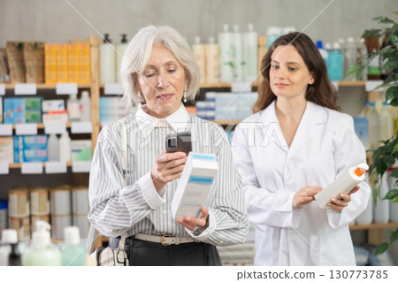 Mature woman in pharmacy scans QR code on cream, woman pharmacist in background 130773785