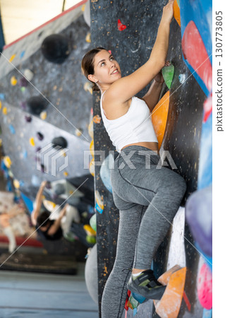 Female fitness climber training at bouldering gym. Young woman rise up on artificial climbing wall 130773805