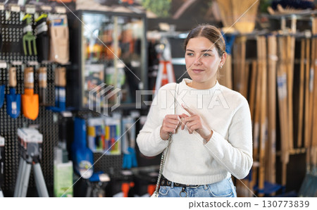 In hardware store department, young woman looking for something on shelf of showcase 130773839