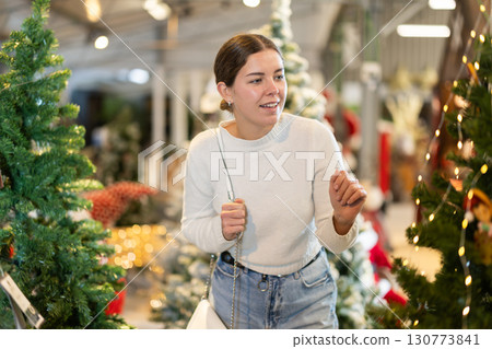 Girl in store examines artificial Christmas tree, examining details of product 130773841