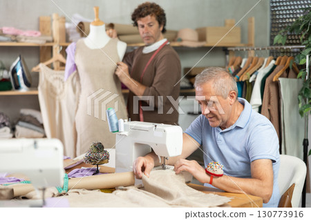 mature woman sews against the background of a tailor and a mannequin mature woman sews against the background of a tailor and a mannequin 130773916